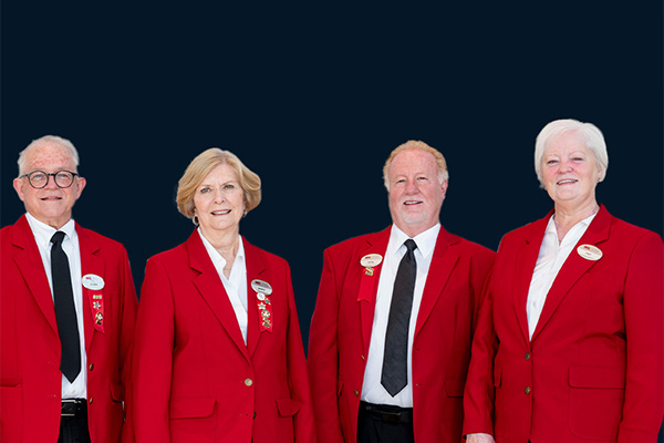 Four people in matching red blazers and name badges standing side by side against a dark background.